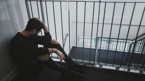 Full length of depressed man sitting by railing in building