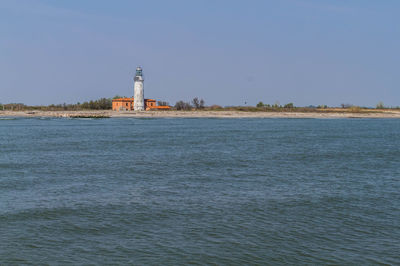 Lighthouse by sea against clear sky