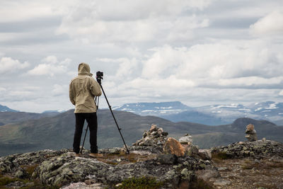 Rear view of man photographing on cliff against cloudy sky