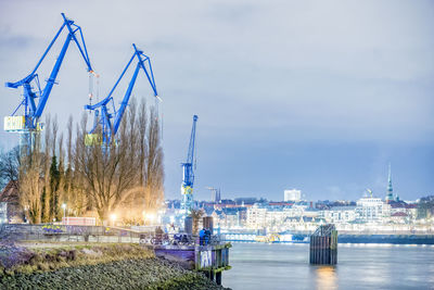 Cranes at harbor by city during dusk