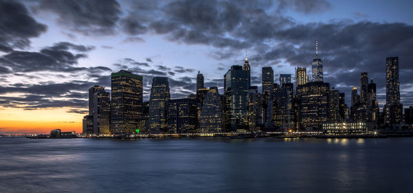 Illuminated buildings by sea against sky at dusk