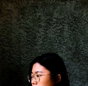 Close-up portrait of woman wearing eyeglasses against wall