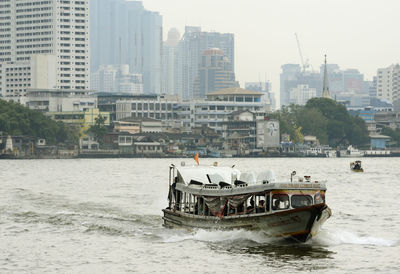 Ferry boat in river against buildings in city