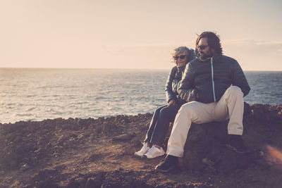 Couple sitting on shore at beach against sky