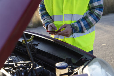 Adult man holding his car hood open and texting a mechanic because his car broke down 