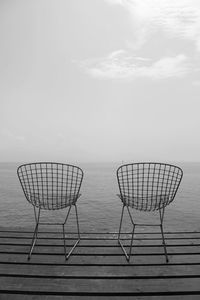 Deck chairs by sea against sky during sunset