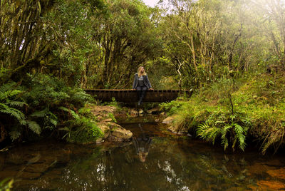 Smiling woman sitting on footbridge over lake 