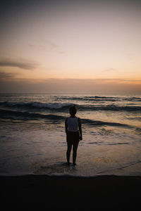 Rear view of woman standing on beach watching sunset 