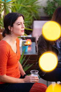 Side view of woman holding drink looking away while sitting outdoors