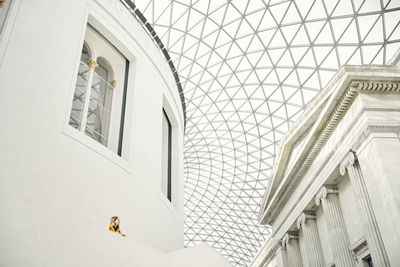 From below female standing on terrace outside white ornamental building and admiring geometric dome ceiling inside modern pavilion