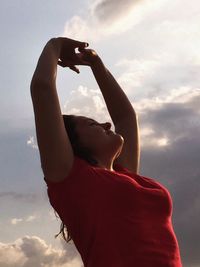 Low angle view of happy woman standing with arms raised against sky