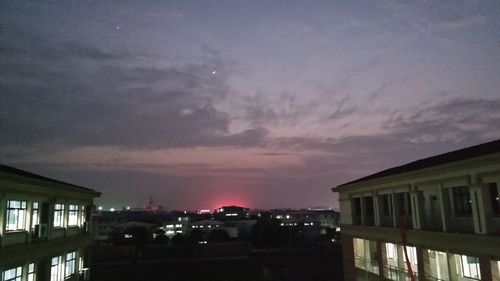 Illuminated houses against dramatic sky at sunset