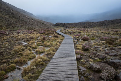 Narrow footpath leading towards mountain against sky