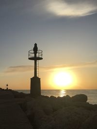 Silhouette lighthouse on beach against sky during sunset
