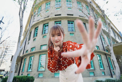 Portrait of young woman standing against building