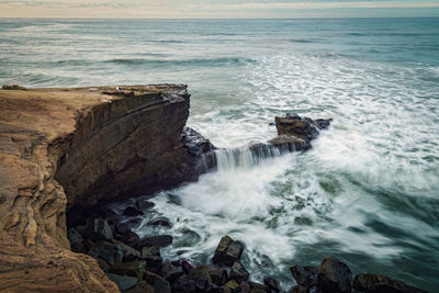 Long exposure surf crashing against beach bluffs on a cloudy day