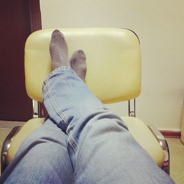 person, low section, indoors, shoe, personal perspective, relaxation, jeans, sitting, lifestyles, casual clothing, footwear, human foot, legs crossed at ankle, home interior, chair, sofa, resting