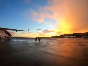 People at airport against sky during sunset