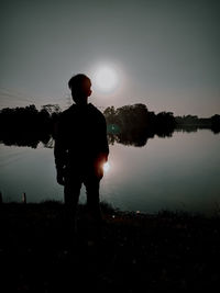 Silhouette man standing by lake against sky during sunset