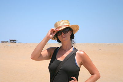 Portrait of woman wearing sunglasses standing on beach against clear sky