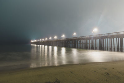 Illuminated bridge over sea against sky at night