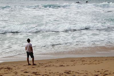 Rear view of man standing on shore of beach