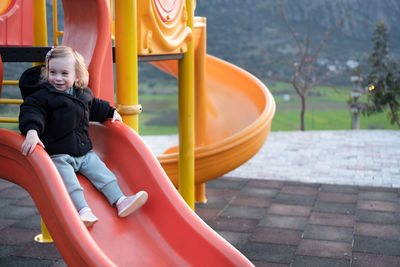 Happy girl,toddler in warm clothes sliding on playground.kid infant leisure time outdoors lifestyle