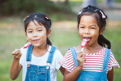 Portrait of happy girls eating popsicles at park