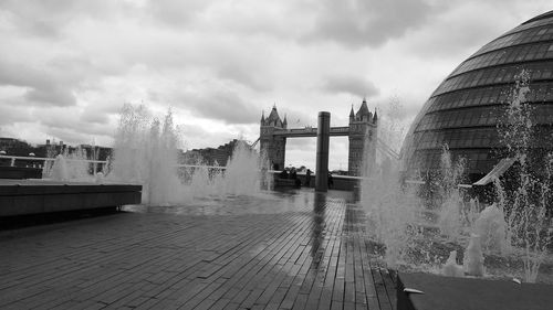 Fountain in city against sky and london tower bridge in background 