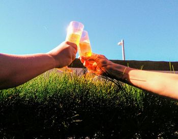 Close-up of hand holding grass against clear blue sky