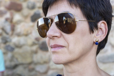 Close-up of woman wearing sunglasses against wall