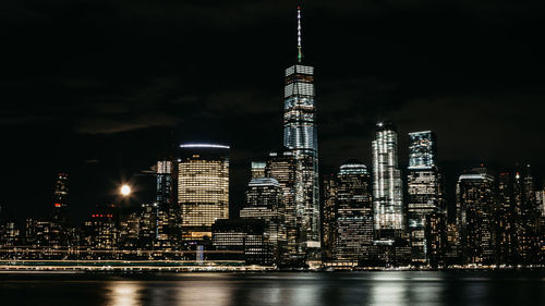 Illuminated buildings by river against sky in city at night