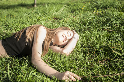 Close-up of smiling woman lying on grass at field on sunny day