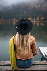 Close up of traveler female sitting on a pier near the wilderness forest in autumn season.	