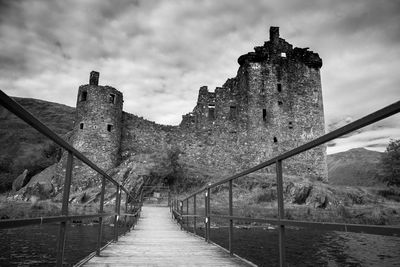 Narrow footbridge leading towards tower against sky