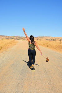 Full length of woman with arms raised against clear sky