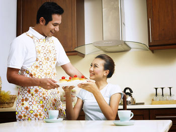 Happy mid adult couple holding cupcakes in plate at kitchen