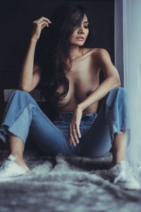 Shirtless young woman sitting on bed at home