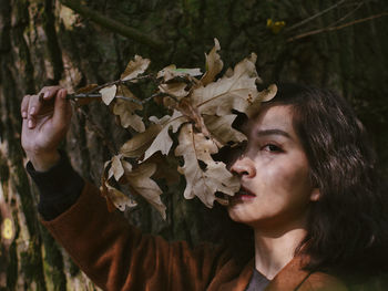 Close-up portrait of young woman holding dry leaves