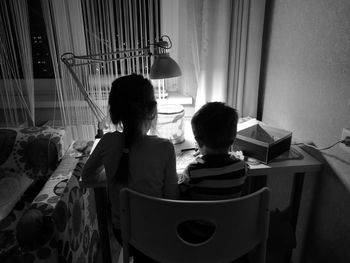 Rear view of sibling drawing at table in home