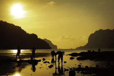 Silhouette people on beach against sky during sunset
