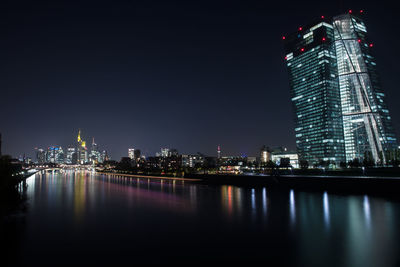 Illuminated city by river against sky at night