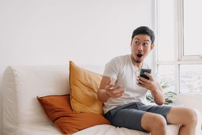 Young woman using mobile phone while sitting on bed at home