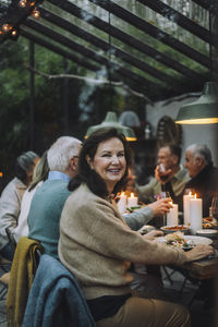 Portrait of happy retired woman sitting on chair during dinner party with friends