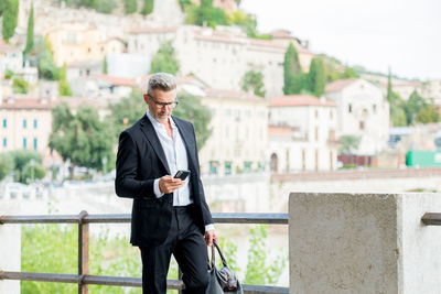 Businessman using mobile phone walking in city street and commut to work texting on smartphone