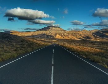 Empty road by mountains against sky