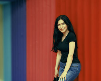 Portrait of smiling young woman standing against red wall