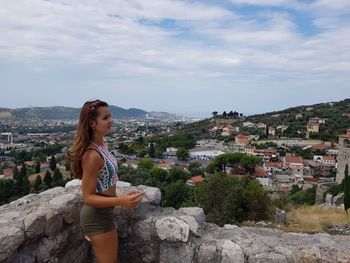 Young woman standing by tree against buildings in city