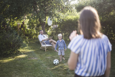 Father looking at son playing football with daughter at back yard