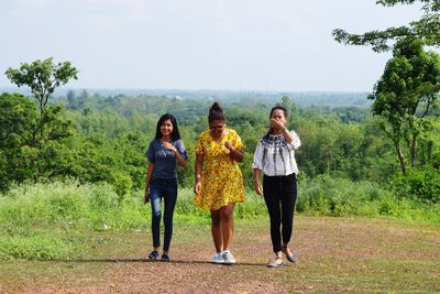 Full length of friends walking on field against sky